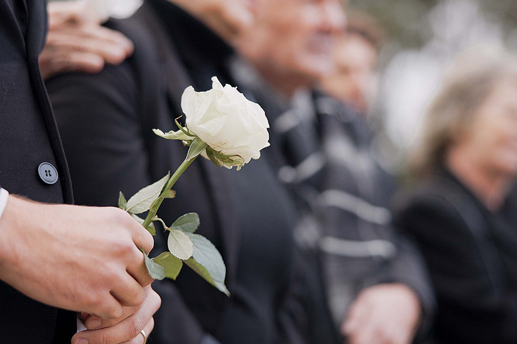 Une personne en deuil tenant une rose blanche lors d'un enterrement dans un cimetière.