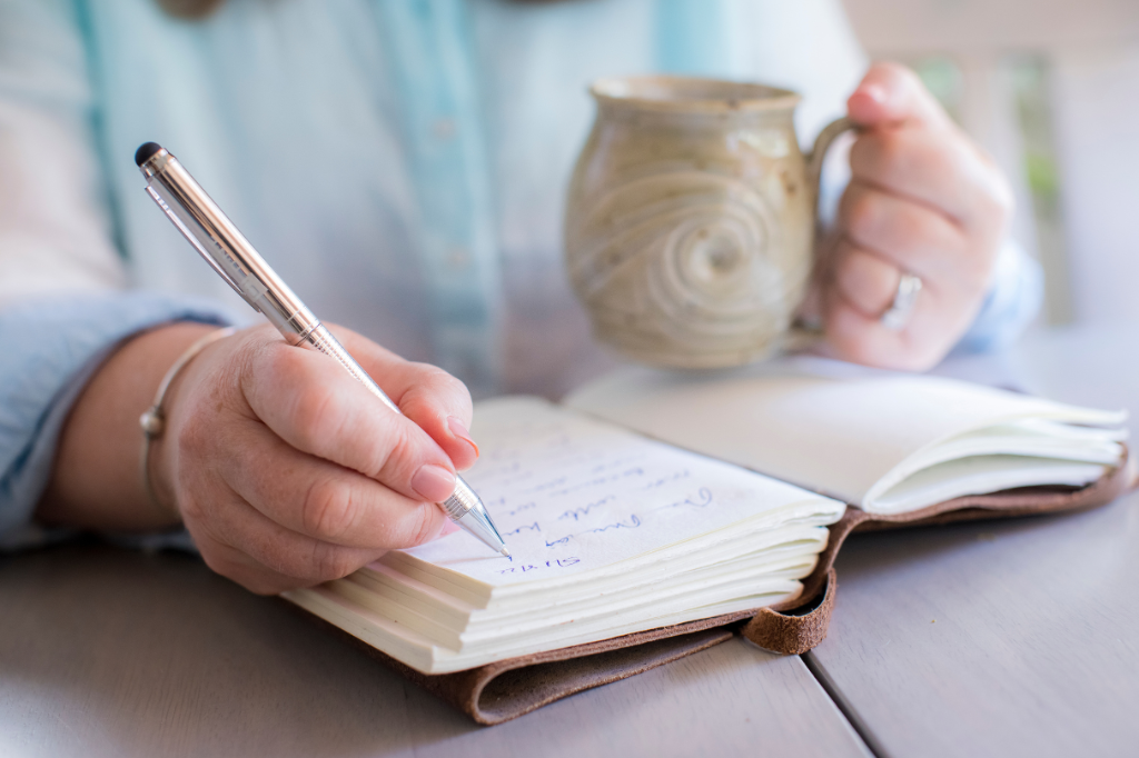 Une proche aidante écrit de la main droite dans un carnet et tient une tasse dans la main gauche