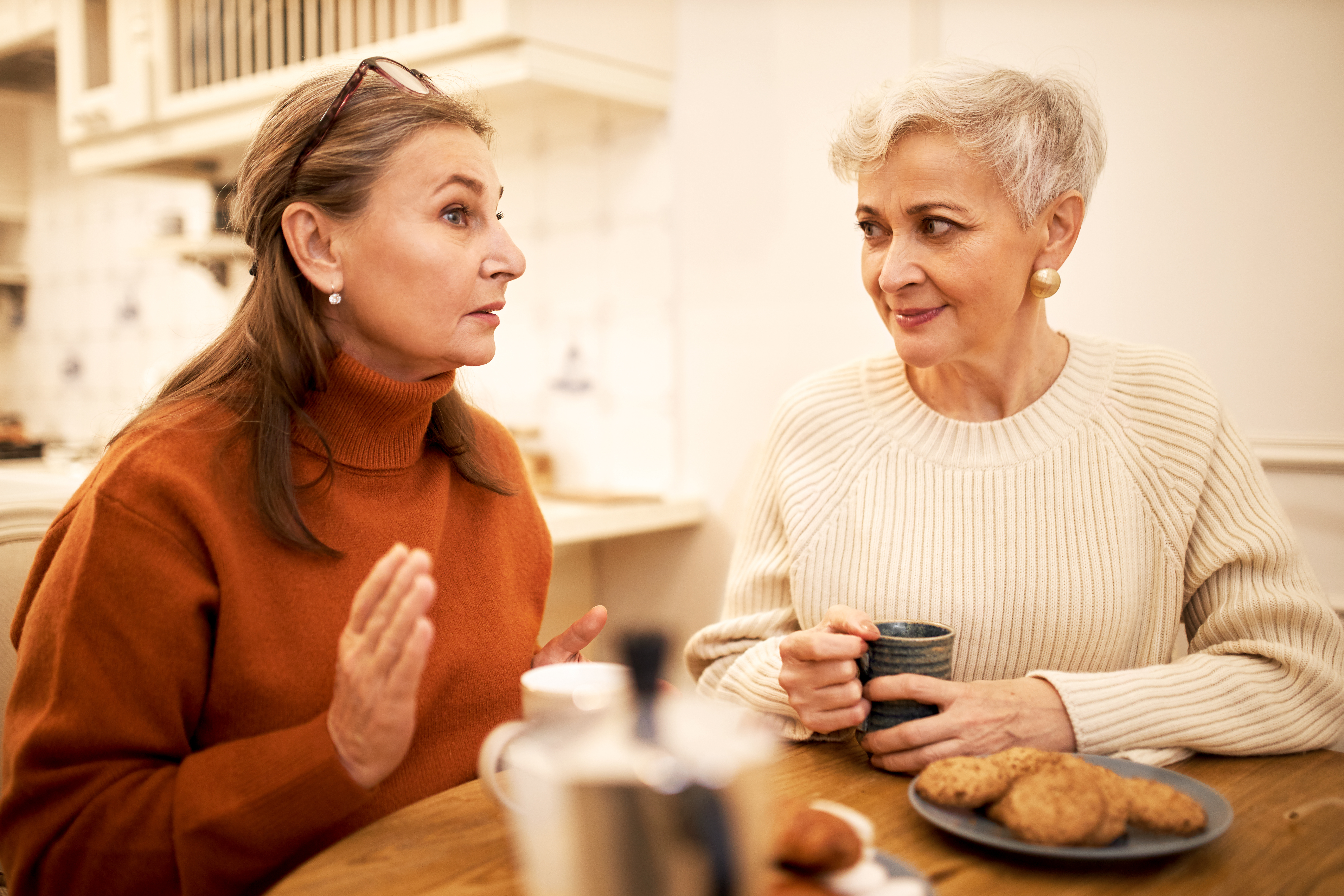 Deux femmes d'âge moyen discutent autour de la table d'une cuisine.