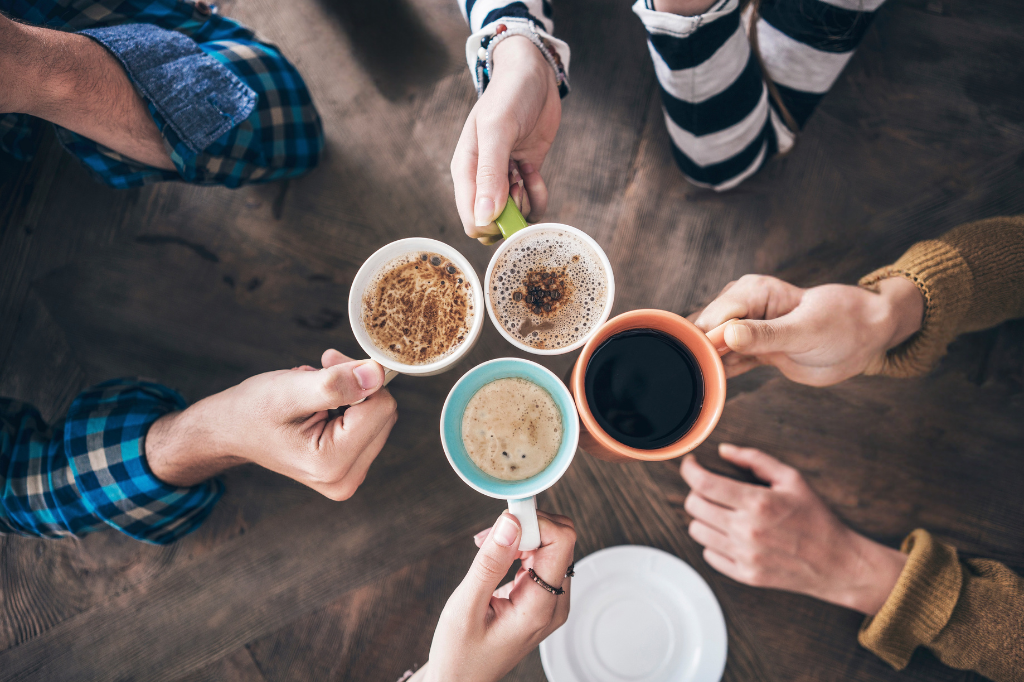 Quatre personnes proches aidantes tiennent leur tasse de café au-dessus de la table, bras tendus vers le centre.
