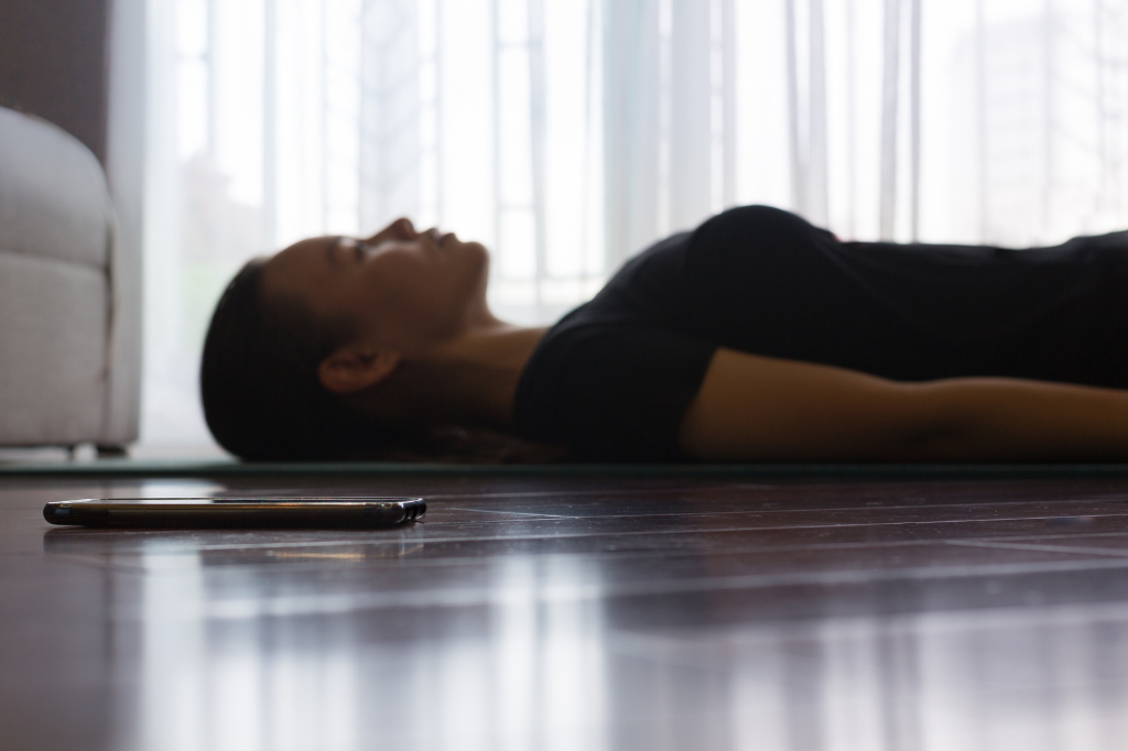 Une proche aidante, couchée sur un petit matelas, suit une méditation guidée dans son salon.
